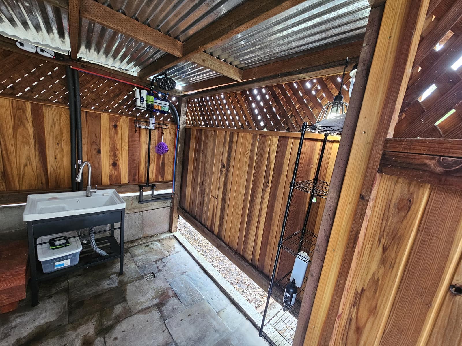 Redwood bath house with a sink, open shower, and lattice walls.
