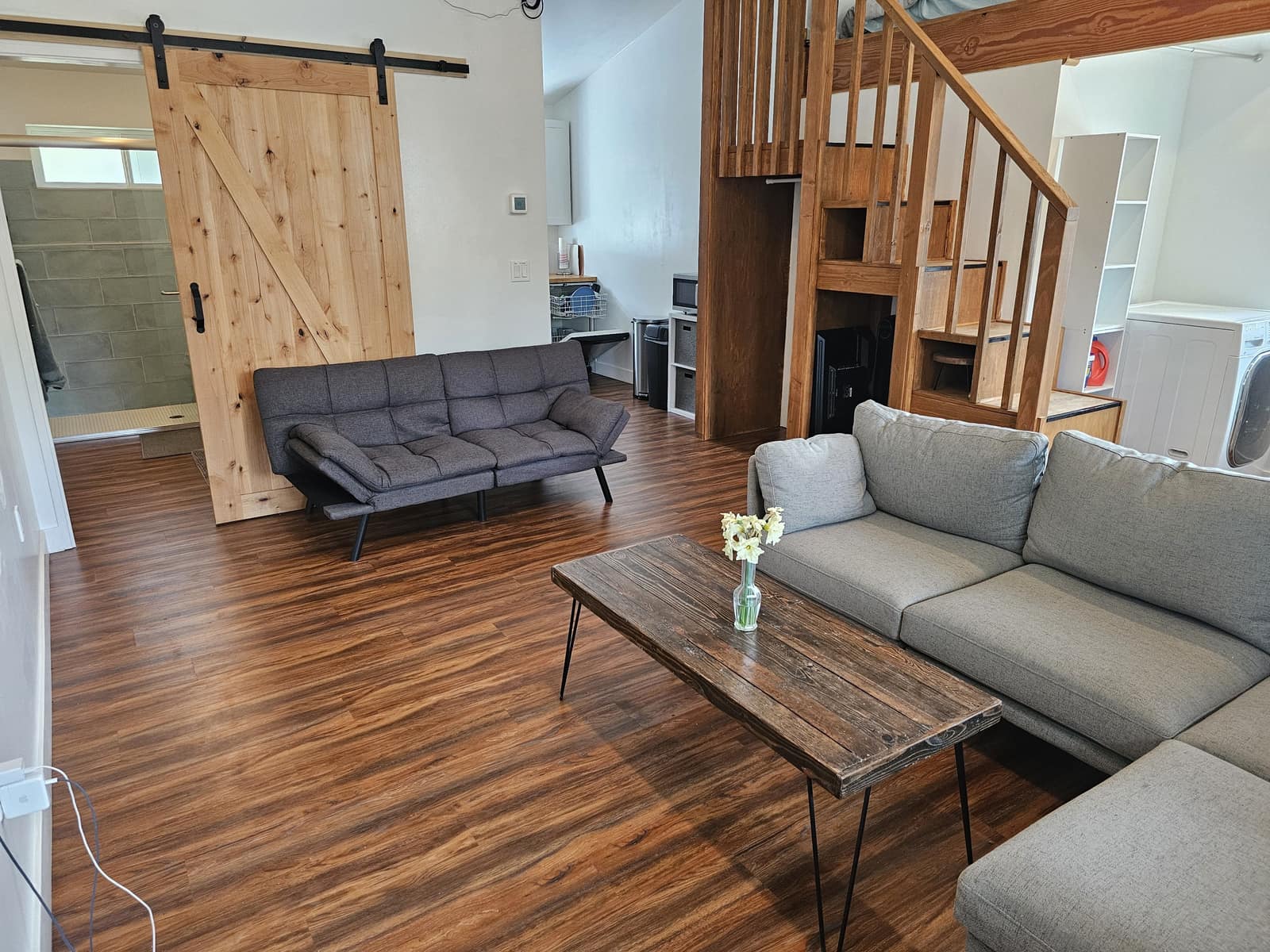 Living room in Unit A with a gray sectional, wood stairs to the loft, and a barn door.