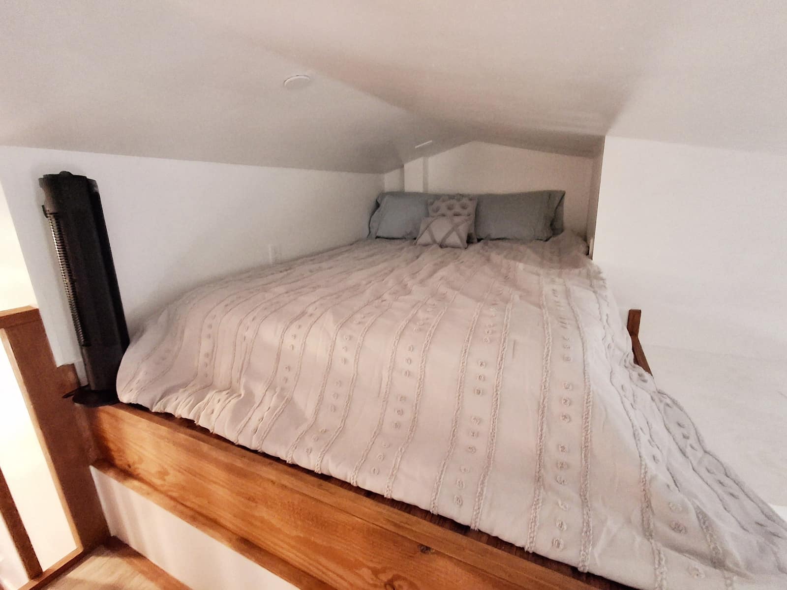 Sleeping loft in The Nest with a white quilt under a sloped ceiling.