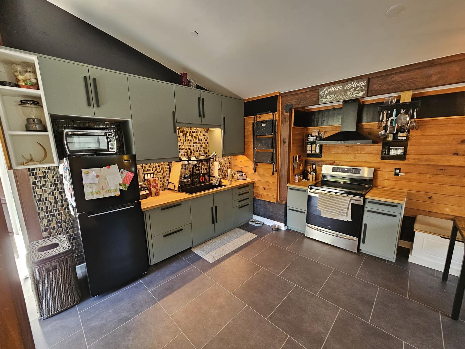 Kitchen in The Den with sage cabinets, a wood wall, and a Griscom Home sign.
