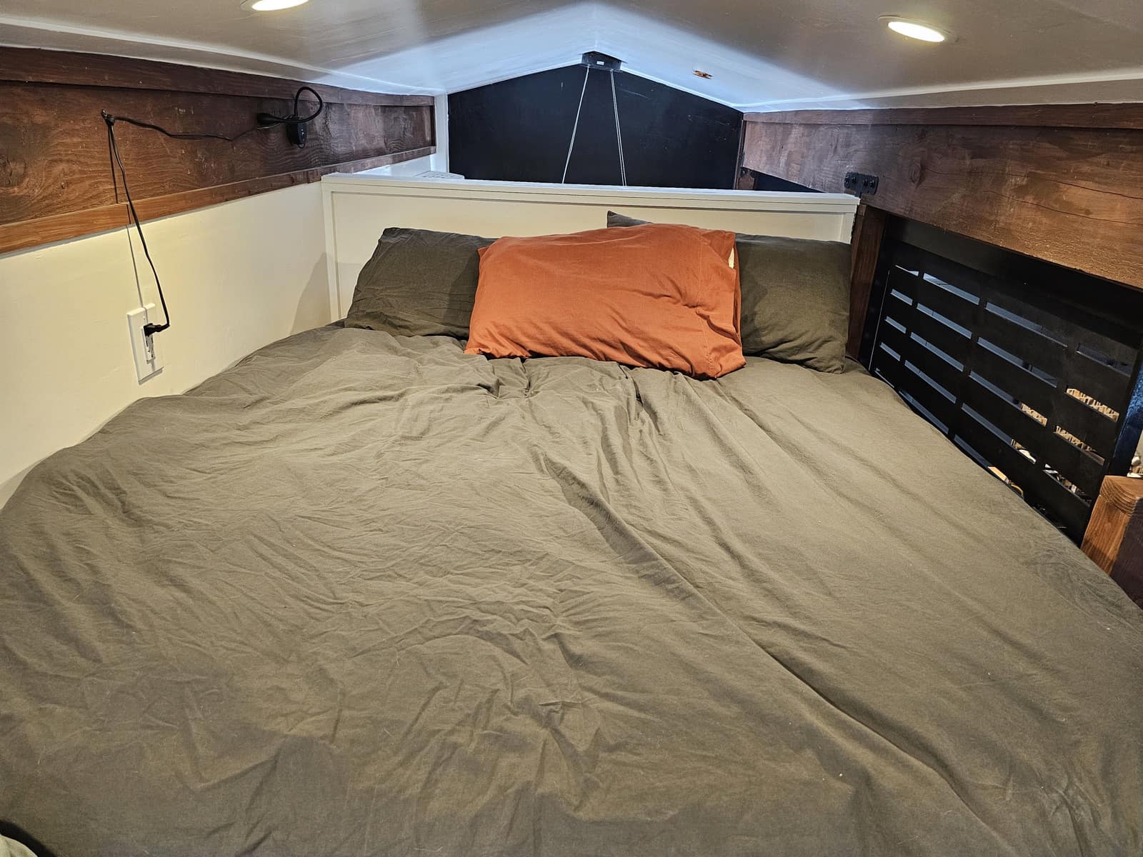 Sleeping loft in The Den with dark bedding under wood beams.